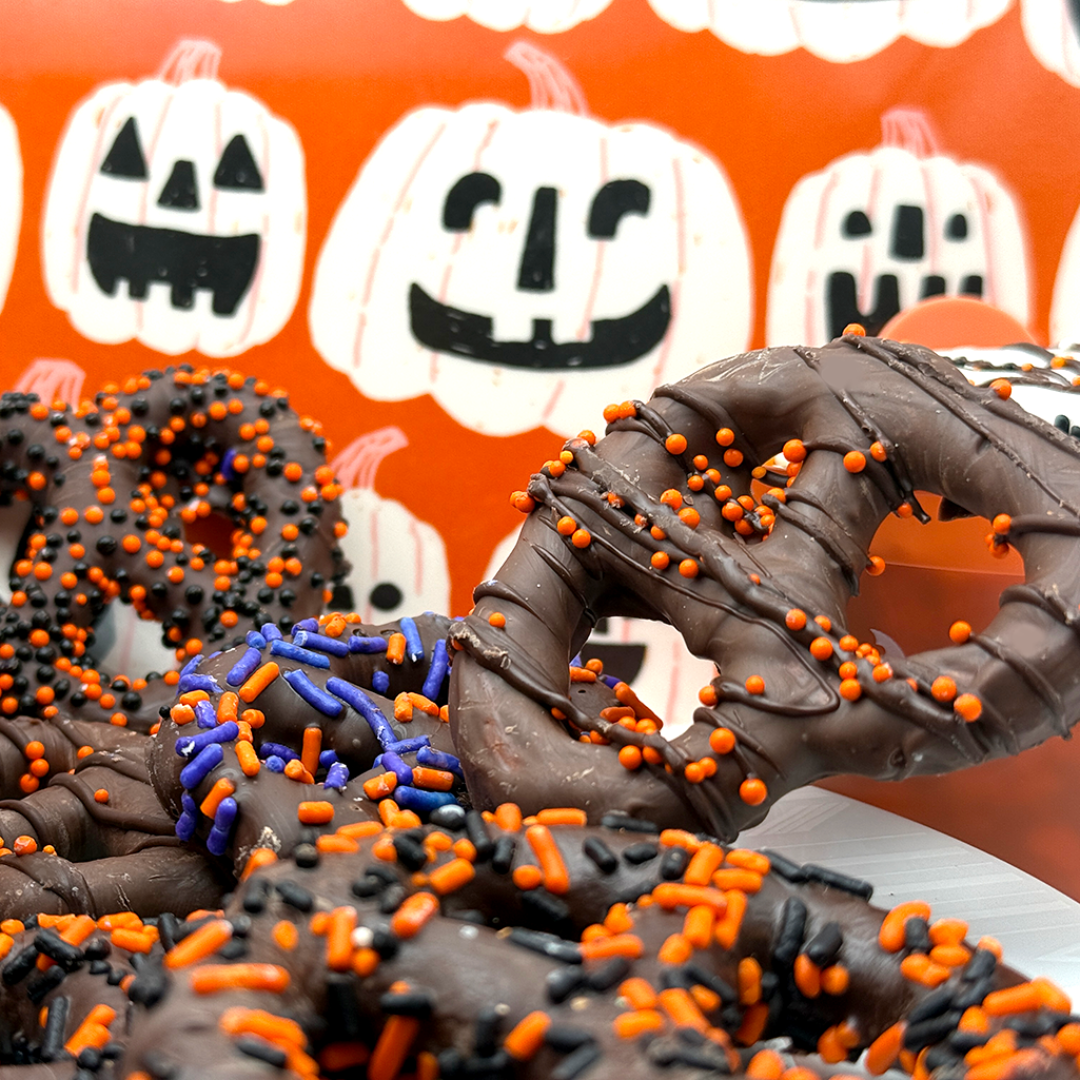 Chocolate-dipped treats with orange and black sprinkles on a Halloween-themed background